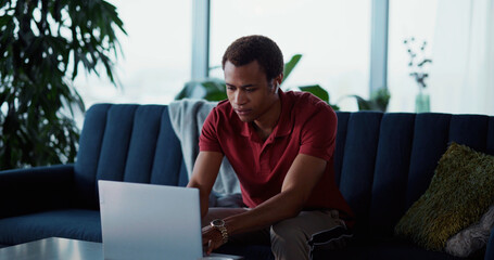 Young handsome afro-american man using laptop computer portable device for freelance work staying home in living room. Ethnicity. Modern people.