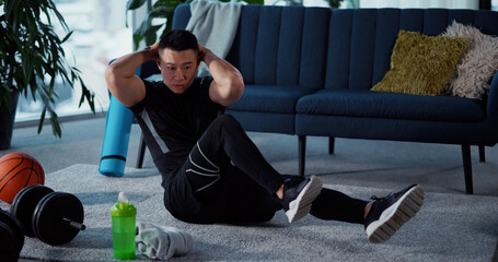 Chinese young man sports guy doing twist core exercise at home. Asian bodybuilder warming up home...