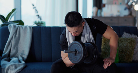 Fototapeta na wymiar Portrait of Handsome Strong Japanese Young Man in Sportswear Sitting on Sofa in Living Room Lifting Heavy Black Dumbbell SMiling to Camera.