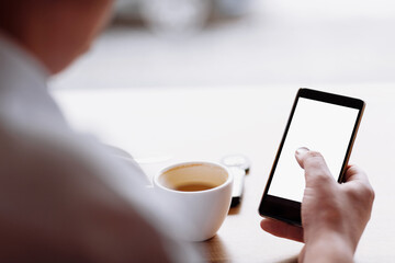 businessman hand holding a phone with isolated screen against moke up and drink coffee in the coffee shop blurred coffee cup background, Mock up concept