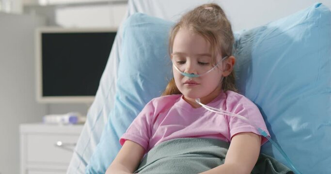 Girl suffering from pneumonia lying in hospital bed with oxygen nasal tube