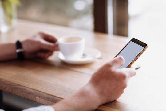 businessman hand holding a phone with isolated screen against moke up and drink coffee in the coffee shop blurred coffee cup background, Mock up concept