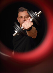 Fototapeta na wymiar Handsome strong sporty man doing the exercises with dumbbells on dark black shadow background in blur red ring Closeup