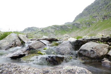 Naklejka na ściany i meble Wasser fließt über Steine einen Bergbach hinunter 
