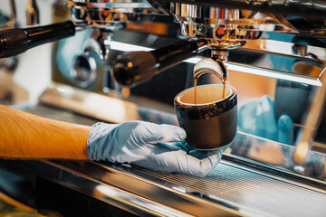 Man's hands prepares coffee, fresh espresso pours into porcelain cup. Making coffee in coffee machine.