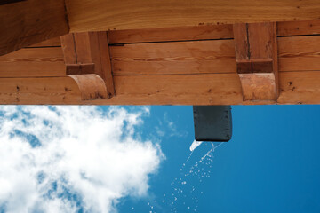 Melted water is pouring from the draining gutter with blue sky background