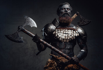 Proud and evil barbarian with two axes posing in dark background