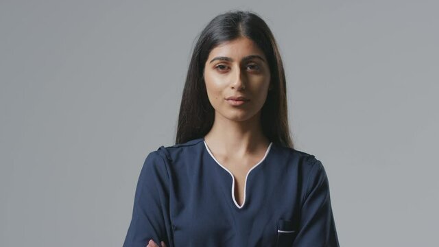 Studio portrait of serious young female nurse in uniform resting face on hand against plain background - shot in slow motion