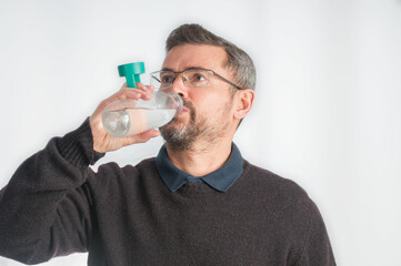 Adult man drinking water from bottle on gray background