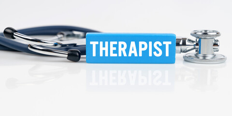 On a white reflective surface is a stethoscope and a blue Jenga with the inscription - THERAPIST