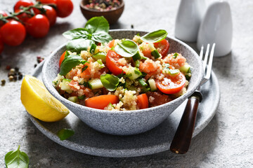 Light salad with tomatoes, cucumber and quinoa with olive oil and basil on a concrete background.