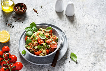 Light salad with tomatoes, cucumber and quinoa with olive oil and basil on a concrete background.