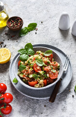 Light salad with tomatoes, cucumber and quinoa with olive oil and basil on a concrete background.