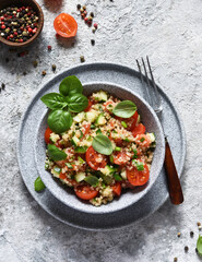 Light salad with tomatoes, cucumber and quinoa with olive oil and basil on a concrete background.