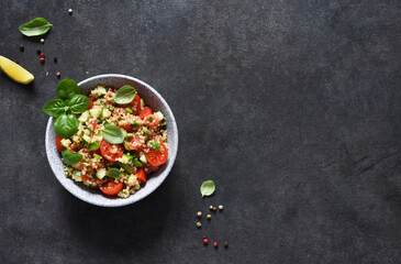 Light salad with tomatoes, cucumber and quinoa with olive oil and basil on a concrete background.