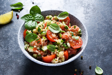 Light salad with tomatoes, cucumber and quinoa with olive oil and basil on a concrete background.