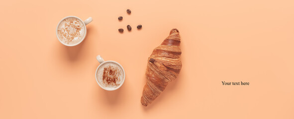 Coffee cups and fresh croissant on a pastel peach color background. Creative layout. Breakfast concept. Top view, flat lay. Banner