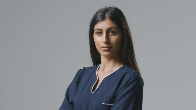 Studio portrait of serious young female nurse in uniform resting face on hand against plain background - shot in slow motion