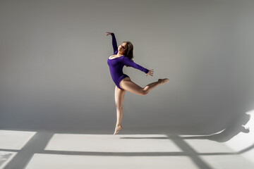 Sexy plus size model with big breasts in purple bodysuit jumping in studio