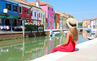 Tourism in Venice. Panoramic banner view of pretty woman in red dress sitting and looking the old colorful town of Burano in Venice, Italy.
