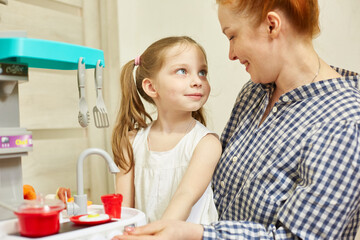 a caring mother plays with her daughter, teaches her the profession of a cook. the girl is very interested in how to cook properly.