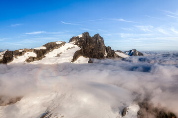 Aerial View from Airplane of Tantalus Range covered in clouds. Blue Sky Art Render. Taken near Squamish, North of Vancouver, British Columbia, Canada. Canadian Nature Background