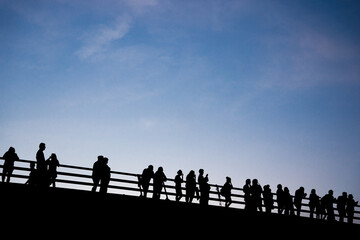 Gente a contraluz parada sobre un puente.  - obrazy, fototapety, plakaty