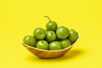 Green olives in eco friendly wooden bowl isolated on yellow background.