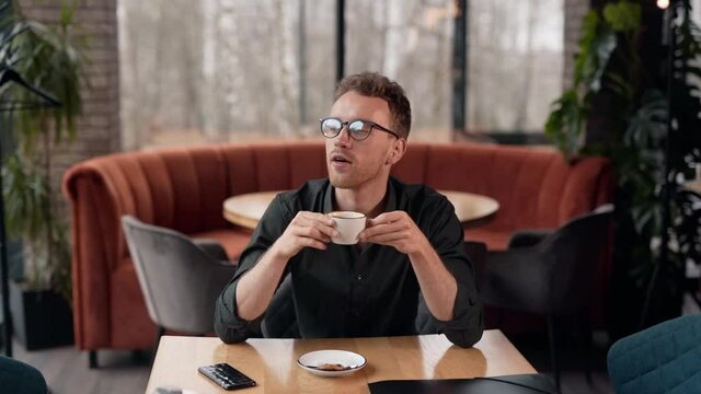 Stylish young man sitting in a cafe receives a joyful message on a smartphone