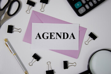 agenda the word is written on a white sheet of paper, pens, scissors, a magnifying glass, paper clips lie next to