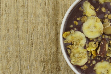 Brazilian açai in a white bowl with banana, granola and chestnuts. Top view. 