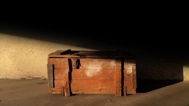 Vertical garage door gate opens to shed light on an old wooden chest against the backdrop of a dirty wall. Treasure hunt