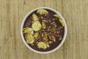 Brazilian açai in a white bowl with banana, granola and chestnuts. Top view. 