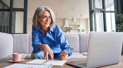 Senior mature older senior adult professional business woman working on laptop from home office,...