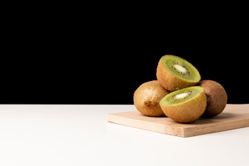 Fresh ripe whole and half kiwi fruit on wooden cutting board against black background.