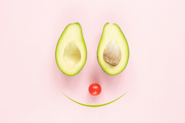 Vegeterian creative smilling concept: two halfs of avocado with and without seed and tomato on pink background.