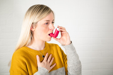 Young blonde woman using a red asthma spray inhaler