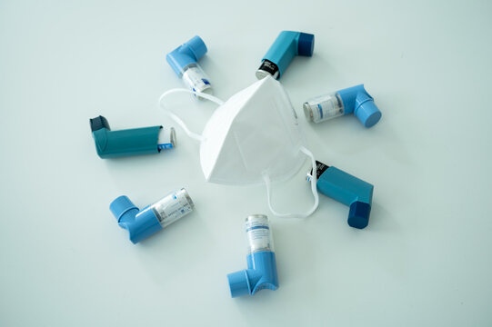 Various asthma spray inhalers and a Covid-19 respirator mask on a white surface