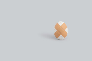 Creative funny Easter concept with broken egg and adhesive bandage on grey background