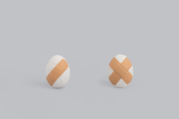 Creative Easter concept with two broken eggs and adhesive bandage on grey background