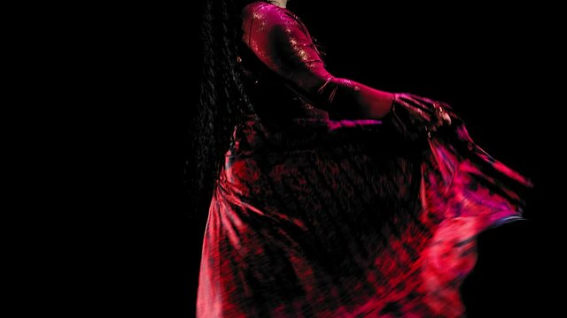 cheerful gypsy woman with long black hair in a red lush dress dances on a black background. Medium plan