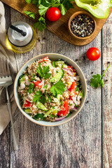 Food dieting concept, tuna salad. Couscous salad with conserved tuna, tomatoes, cucumbers and purple onions on rustic wooden table. Top view flat lay. Copy space.