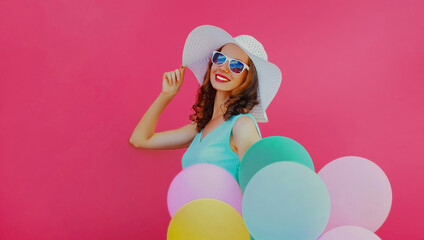 Obraz na płótnie Canvas Portrait of beautiful happy young woman with colorful balloons wearing a summer straw hat on a pink background
