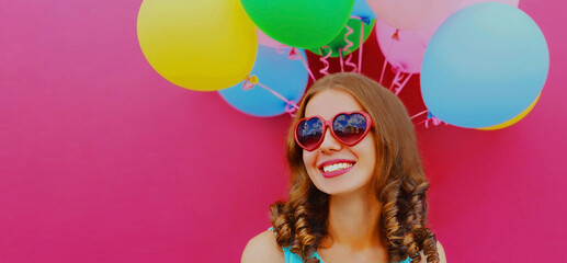 Obraz na płótnie Canvas Portrait of happy smiling young woman with colorful balloons looking away on a pink background