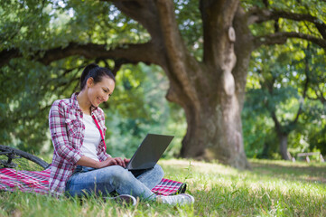 Woman working on laptop computer sitting on a grass in a public park