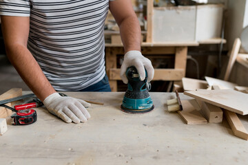 Сarpenter working with wood using electric sander from workshop. Joinery work on the production and renovation of wooden furniture. Small Business Concept. Close up