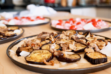 Homemade Italian pizza with eggplant, mushrooms, tomato, cheese and ham in the plate on the table in the kitchen. Selective focus.