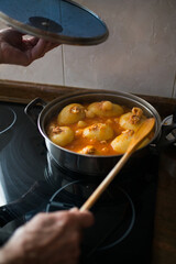 Typical asturian dish. Aged woman's hands with a cooking pot and a wooden spoon while cooking potatoes filled with tuna, tomato and eggs. Gastronomy at home.