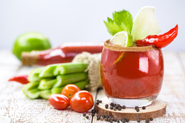 Bloody mary, a red drink based on vodka, tomato juice, lemon juice, celery, peas, Worcestershire sauce, tabasco and pepper, on a white wooden background