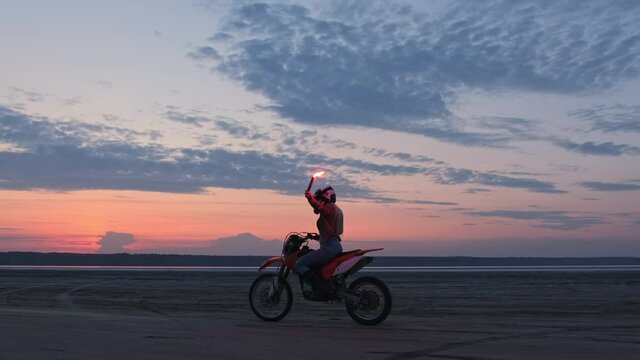 A motocross racer rides a sports bike with a flashing red light after sunset on the beach.